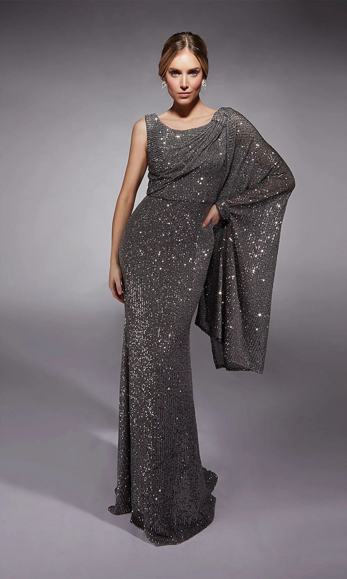 A woman poses in the Alyce 27718 long formal dress in midnight, featuring a chic one-shoulder cape sleeve, against a plain gray backdrop.